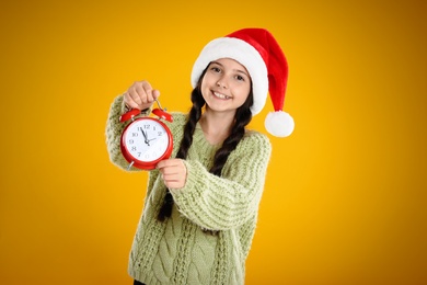 Photo of Girl in Santa hat with alarm clock on yellow background. New Year countdown