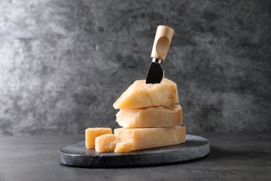 Photo of Parmesan cheese with board and knife on grey table