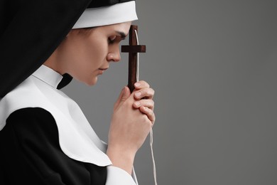 Photo of Nun with cross praying to God on grey background. Space for text