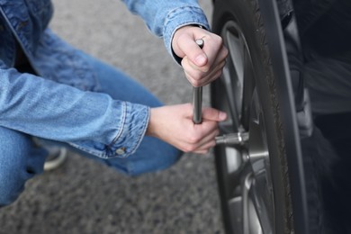 Young man changing tire of car on roadside, closeup
