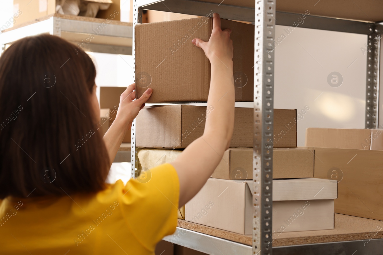 Photo of Post office worker putting box on rack with parcels indoors