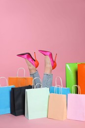 Photo of Happy woman after big sale shopping, her legs sticking out among bright color paper bags on pink background, closeup