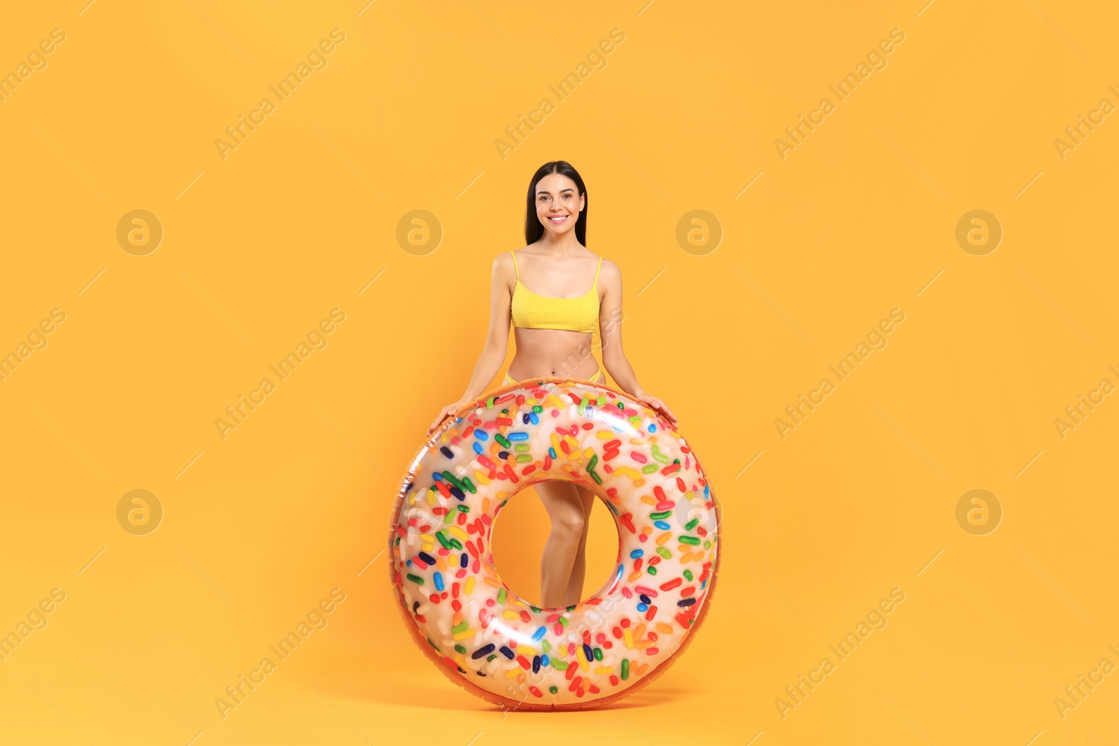 Photo of Happy young woman with beautiful suntan and inflatable ring against orange background