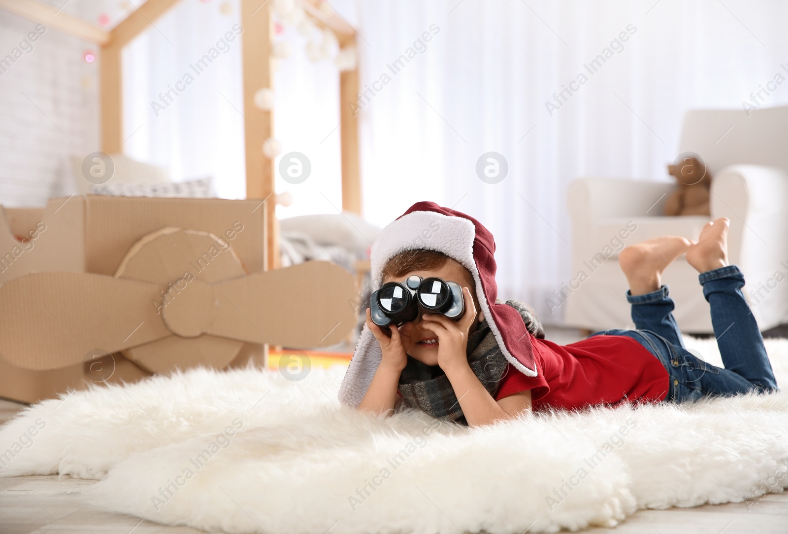 Photo of Cute little boy playing with binoculars and cardboard airplane in bedroom