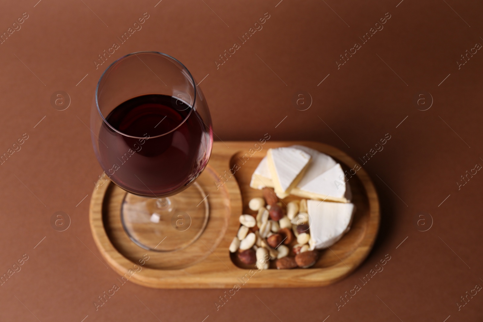 Photo of Glass of red wine, cheese and nuts on brown background