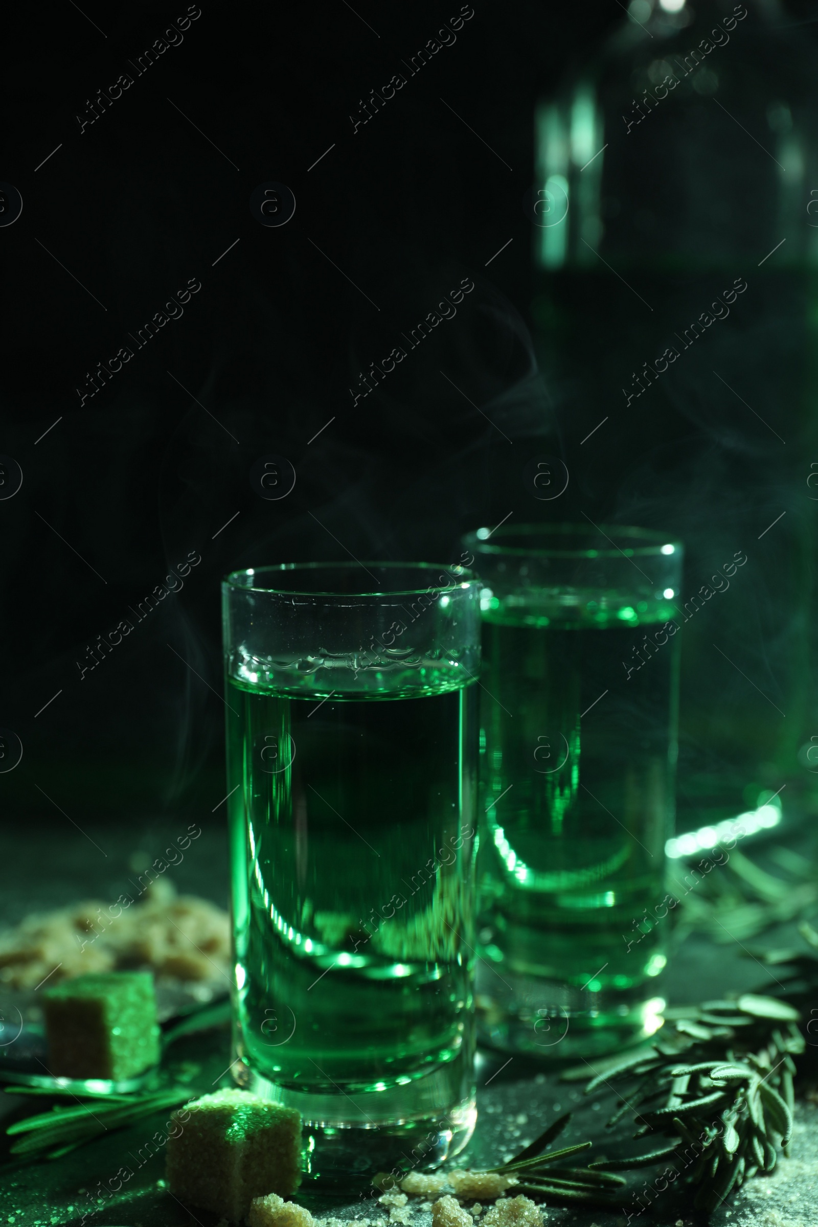 Photo of Absinthe in shot glasses, rosemary and brown sugar on table, closeup. Alcoholic drink