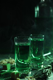 Photo of Absinthe in shot glasses, rosemary and brown sugar on table, closeup. Alcoholic drink