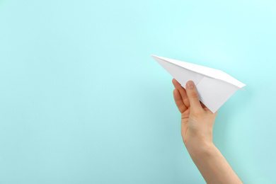 Woman holding paper plane on light blue background, closeup. Space for text