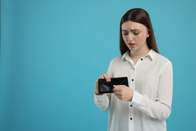 Sad woman showing empty wallet on light blue background, space for text