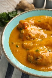 Photo of Tasty chicken curry, parsley and ginger on wooden table, closeup