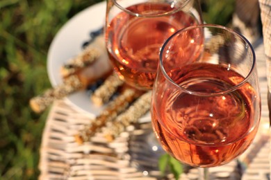 Glasses of delicious rose wine and food on wicker basket outdoors, closeup