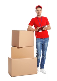 Young happy courier with clipboard near pile of cardboard boxes on white background