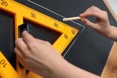 Photo of Woman drawing with chalk and triangle ruler on blackboard, closeup