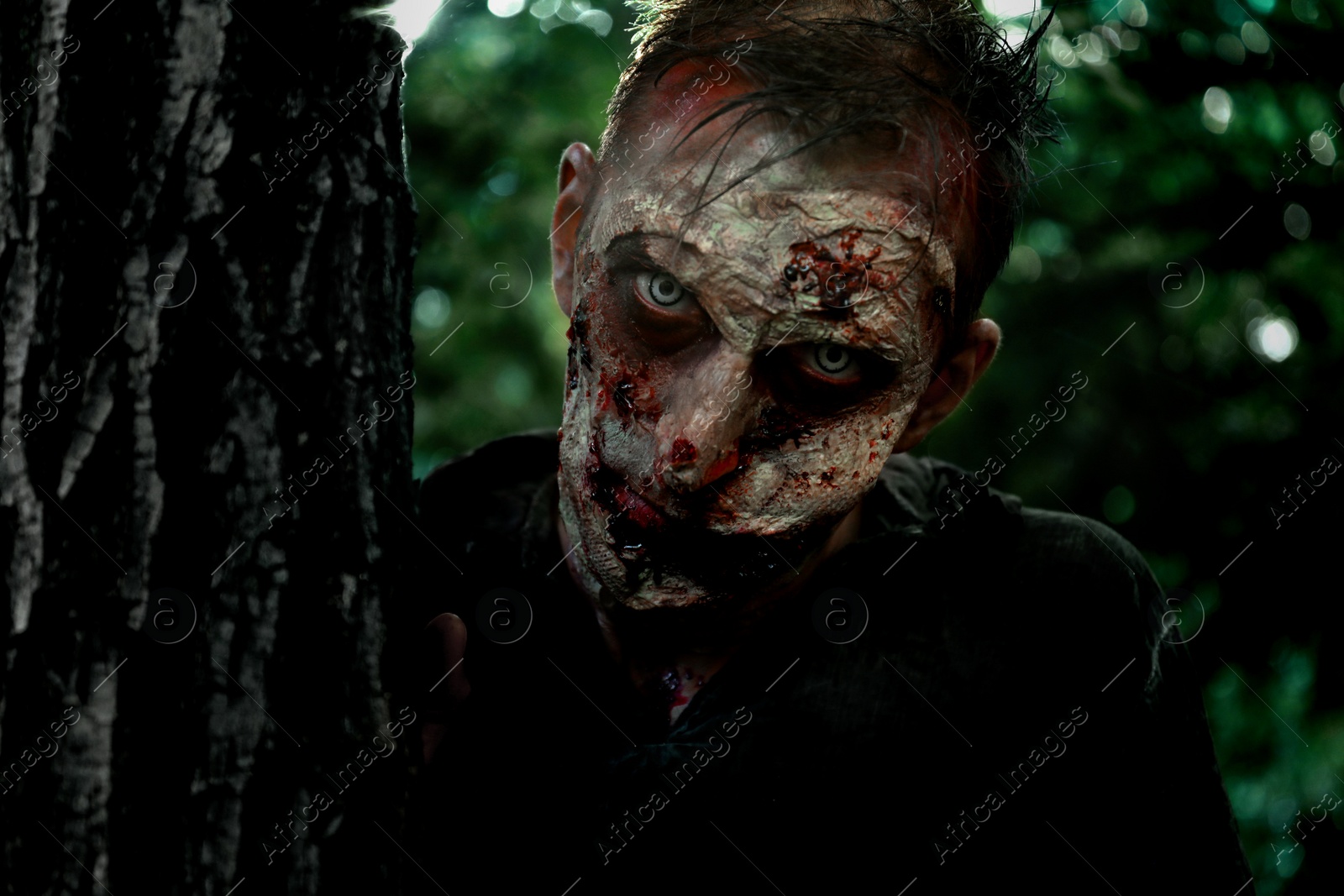 Photo of Scary zombie near tree outdoors. Halloween monster