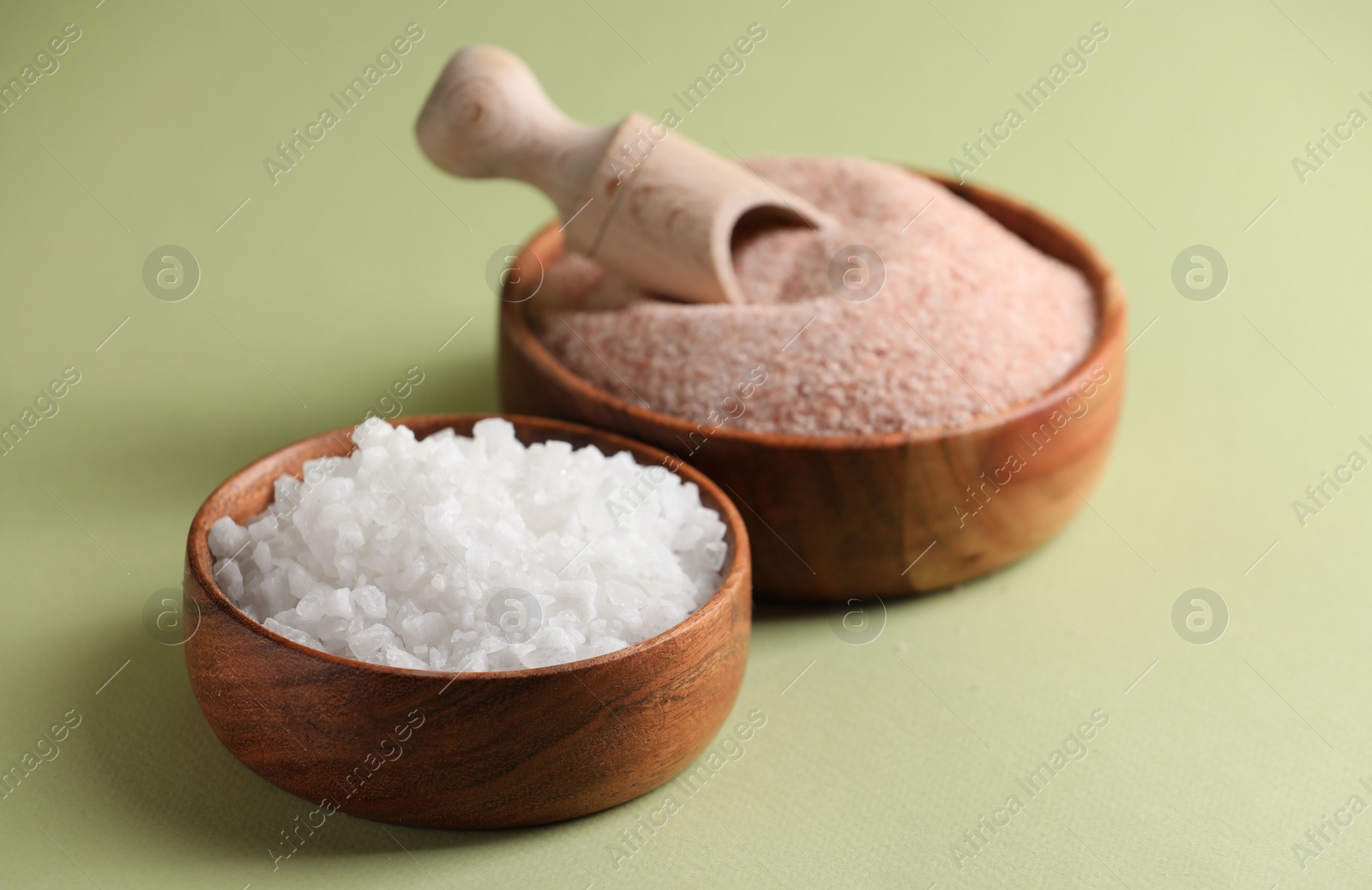 Photo of Different salt in bowls and scoop on green background