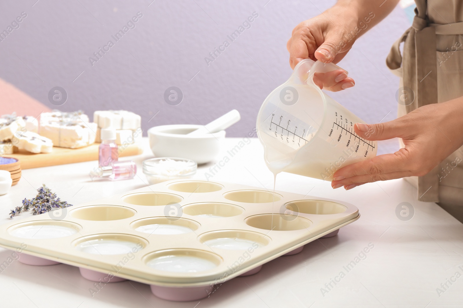 Photo of Woman making hand made soap bar with lavender flowers at table, closeup