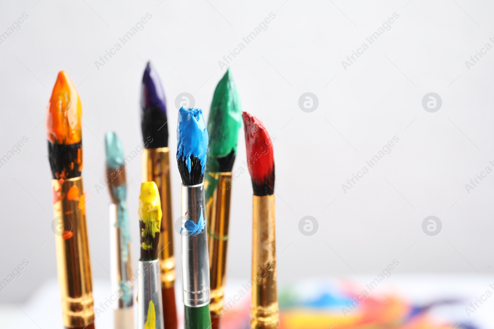 Photo of Brushes with colorful paints on light background, space for text