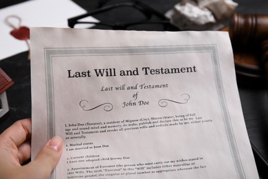 Photo of Woman holding last will and testament at black table, closeup