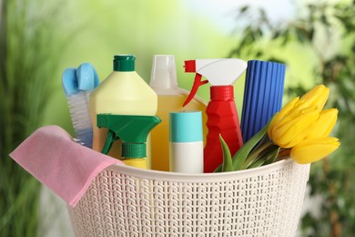 Photo of Spring cleaning. Plastic basket with detergents, supplies and beautiful flowers outdoors