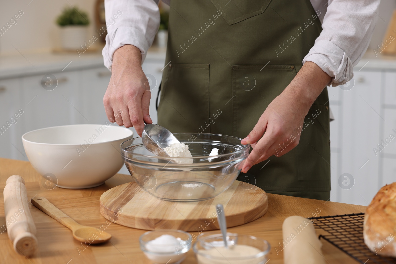 Photo of Making bread. Man putting flour into bowl at wooden table in kitchen, closeup