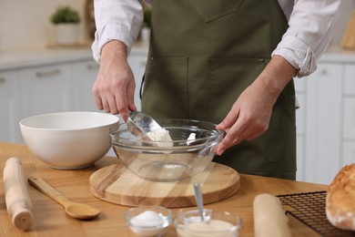 Making bread. Man putting flour into bowl at wooden table in kitchen, closeup