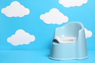 Photo of Baby potty against light blue background with paper clouds, space for text. Toilet training