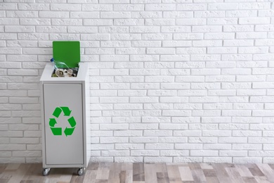 Photo of Overfilled trash bin with recycling symbol near brick wall indoors. Space for text