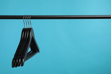 Photo of Black clothes hangers on rack against light blue background. Space for text