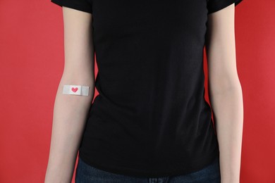 Photo of Blood donation concept. Woman with adhesive plaster on arm against red background, closeup