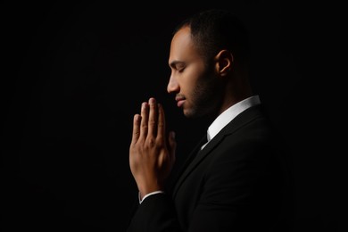 Photo of African American man with clasped hands praying to God on black background. Space for text