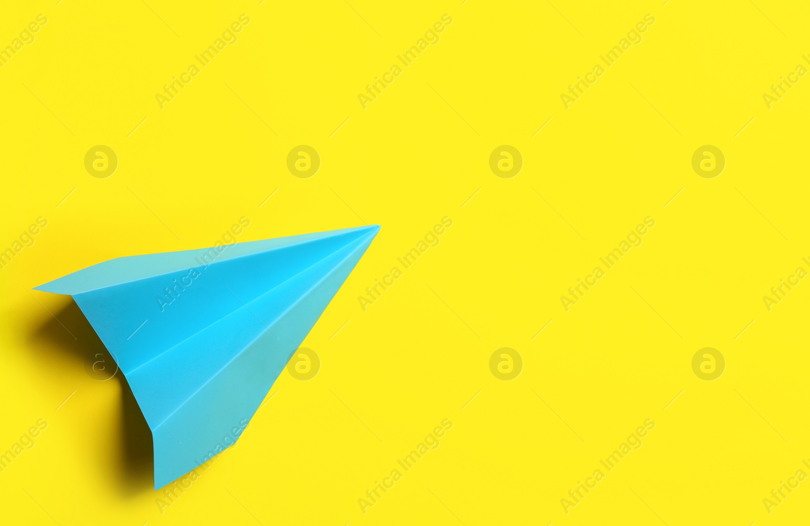 Photo of Light blue paper plane on yellow background, top view. Space for text