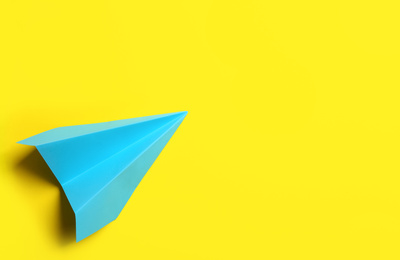 Light blue paper plane on yellow background, top view. Space for text