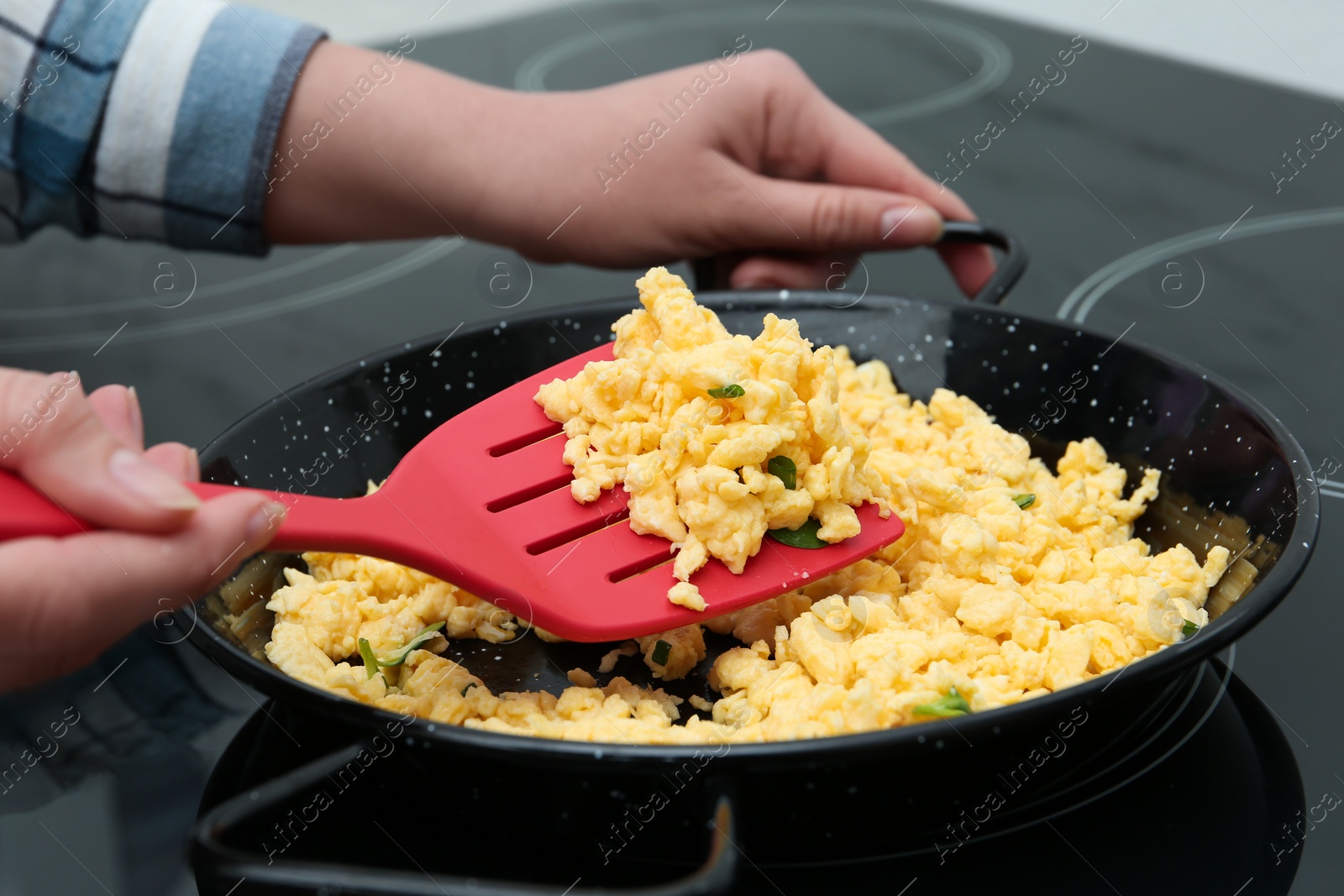 Photo of Woman cooking tasty scrambled eggs in wok pan on stove, closeup