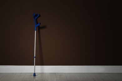 Photo of Elbow crutch near brown wall. Space for text
