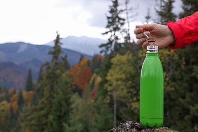 Photo of Woman pouring instant coffee into thermo bottle in mountains, closeup. Space for text