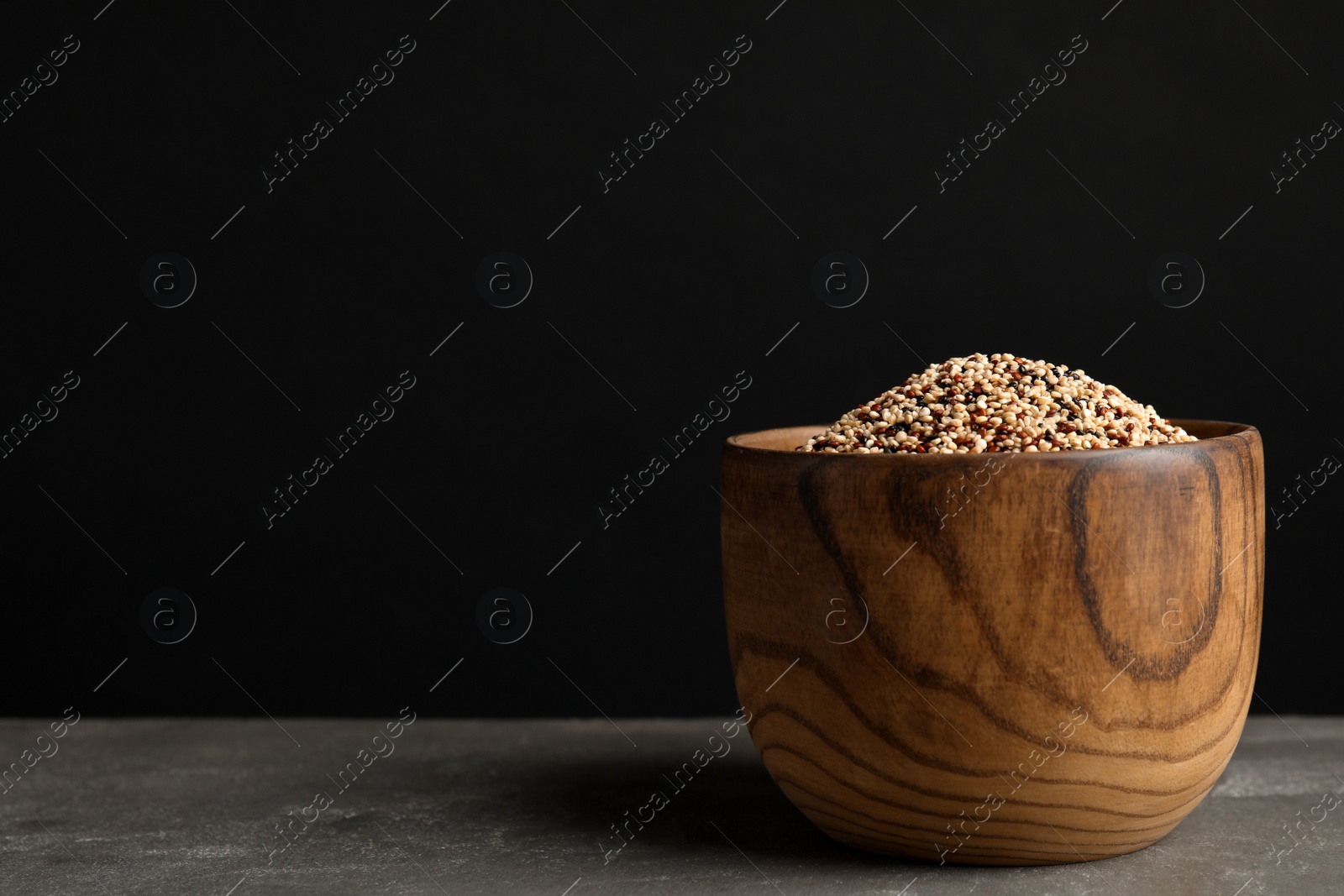 Photo of Bowl with mixed quinoa seeds on table against black background. Space for text