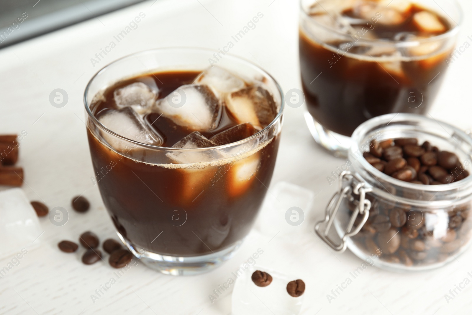 Photo of Glass of coffee drink with ice cubes and beans in jar on table