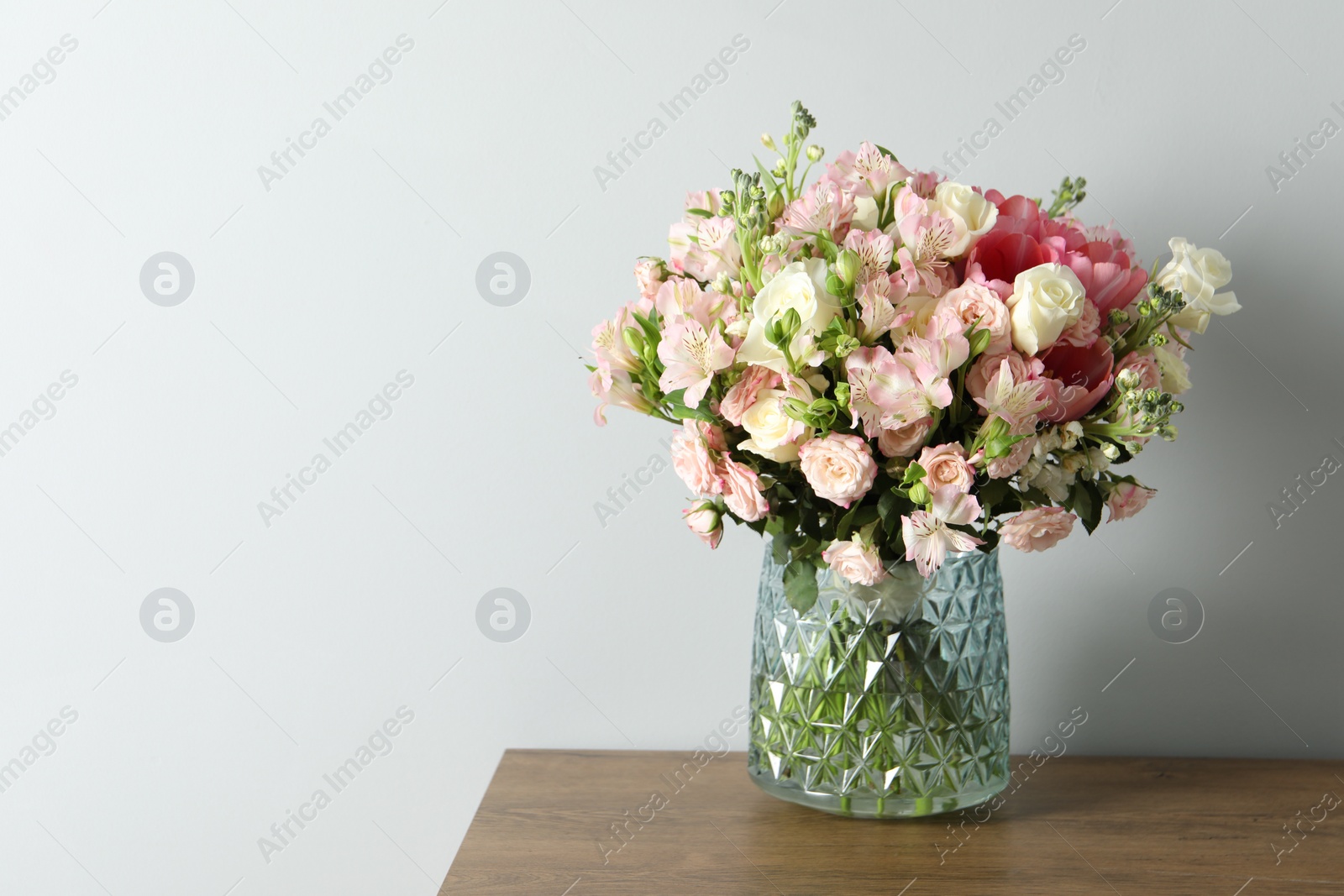Photo of Beautiful bouquet of fresh flowers in vase on wooden table near light wall, space for text