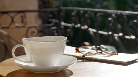 Cup of aromatic coffee, glasses and newspaper on wooden table outdoors. Space for text