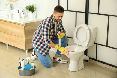 Photo of Young man cleaning toilet bowl in bathroom