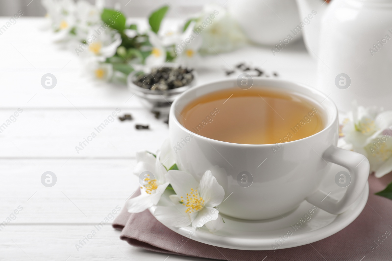 Photo of Cup of tea and fresh jasmine flowers on white wooden table