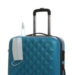 Photo of Stylish blue suitcase, antiseptic spray and protective mask on white background. Travelling during coronavirus pandemic