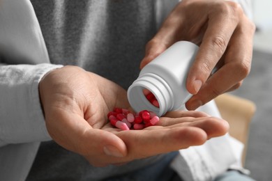 Photo of Man pouring pills from bottle on blurred background, closeup