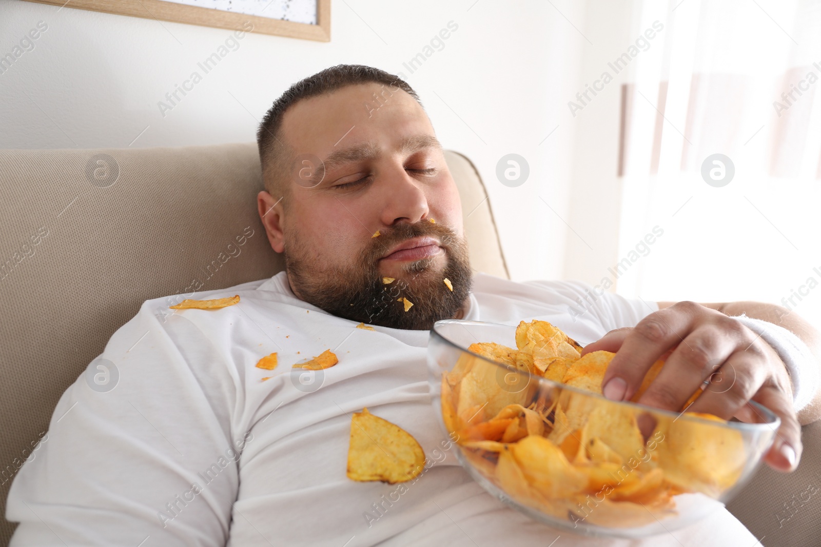 Photo of Lazy overweight man with chips sleeping on sofa at home, closeup
