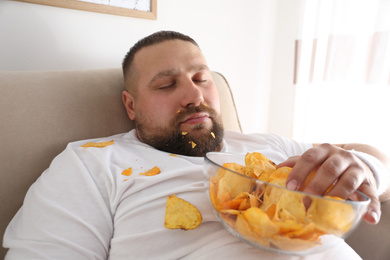 Photo of Lazy overweight man with chips sleeping on sofa at home, closeup
