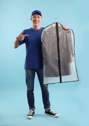 Dry-cleaning delivery. Happy courier holding garment cover with clothes on light blue background