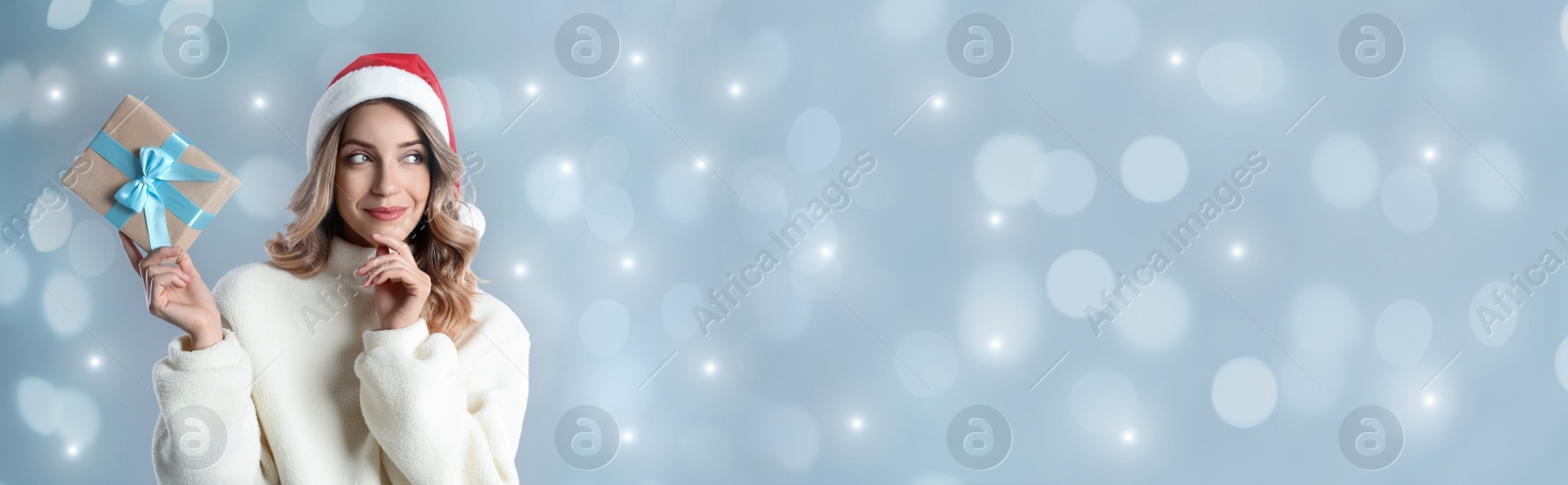 Image of Beautiful woman in Christmas hat holding gift box on light grey background, space for text. Banner design