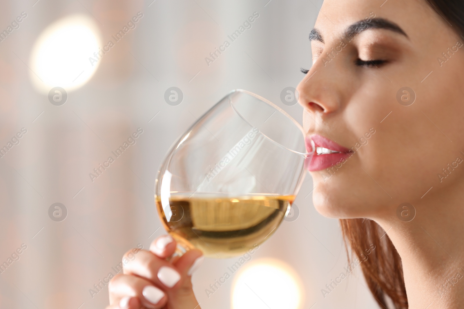 Photo of Beautiful young woman with glass of luxury white wine indoors, closeup view. Space for text