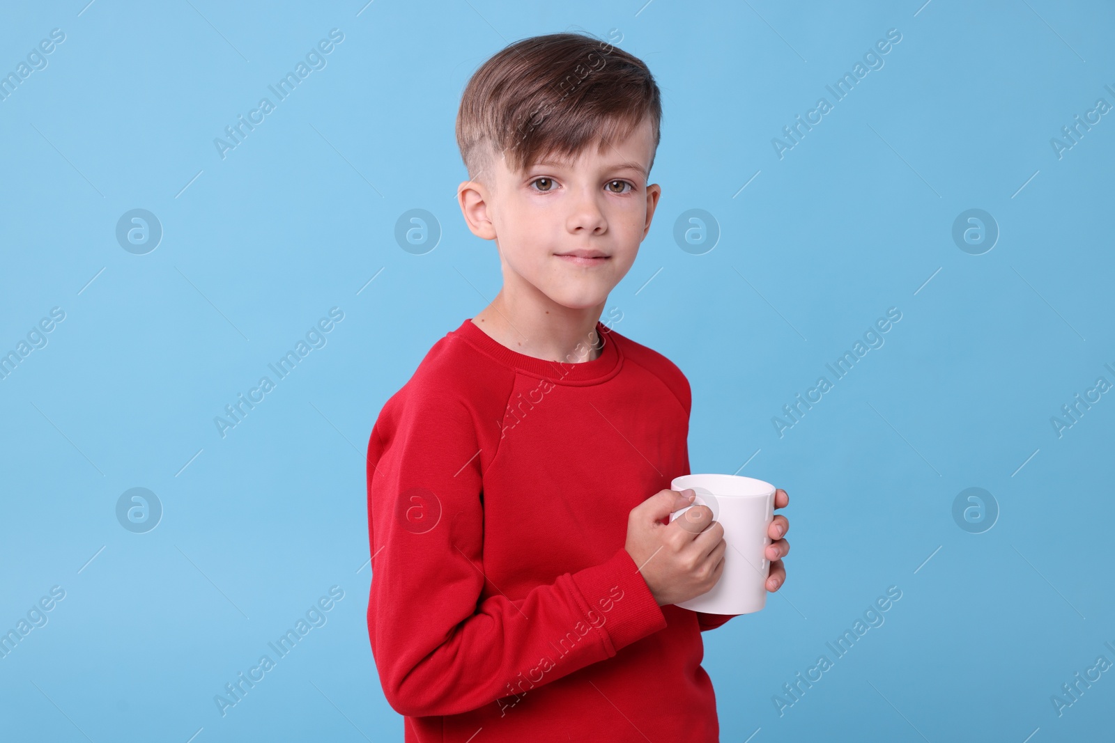 Photo of Cute boy with white ceramic mug on light blue background