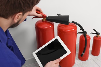 Photo of Man with tablet checking fire extinguishers indoors, closeup